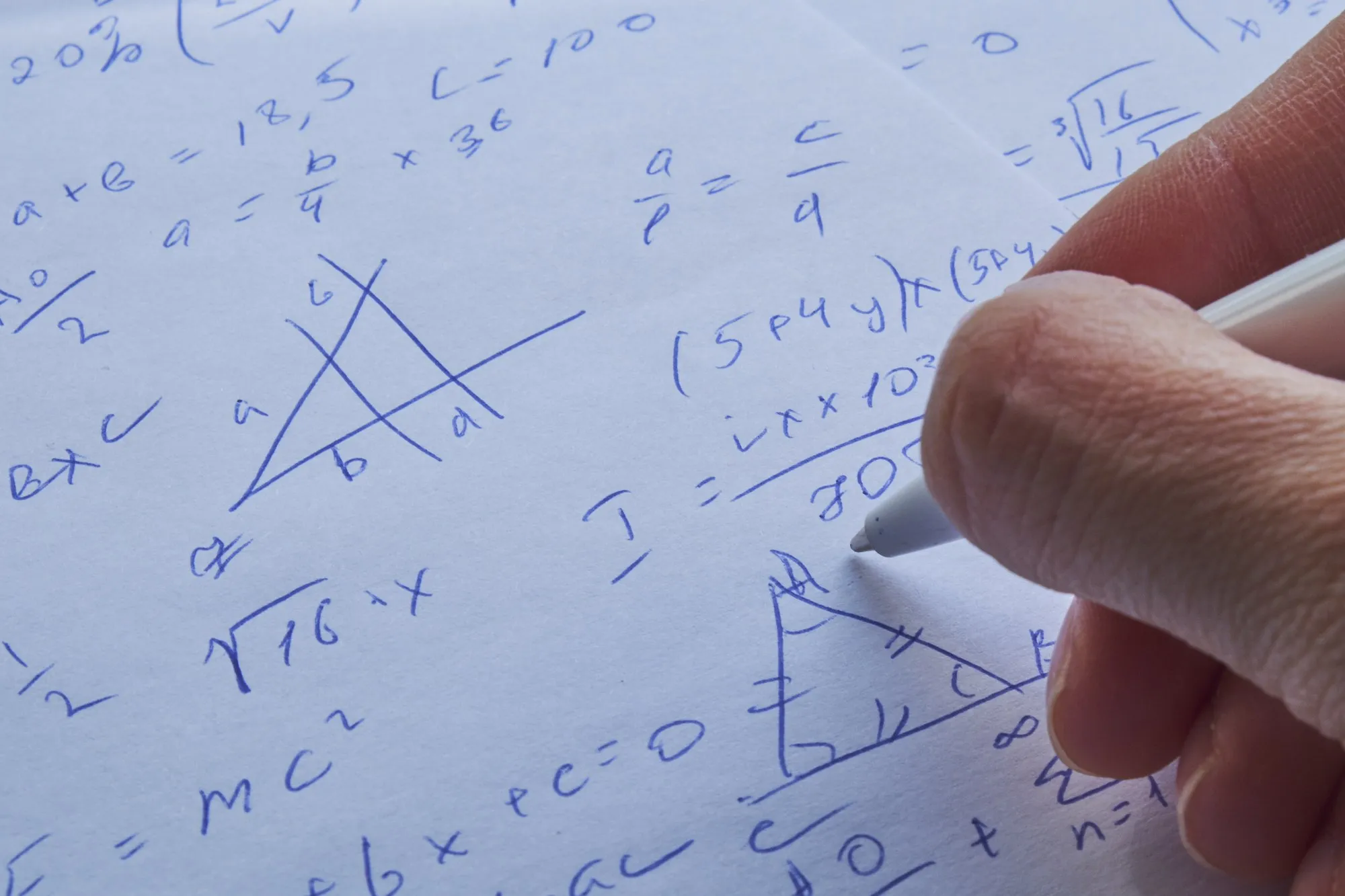 A hand working through equations on paper in blue ink